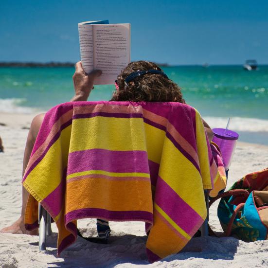 Kvinde ligger og læser på stranden.