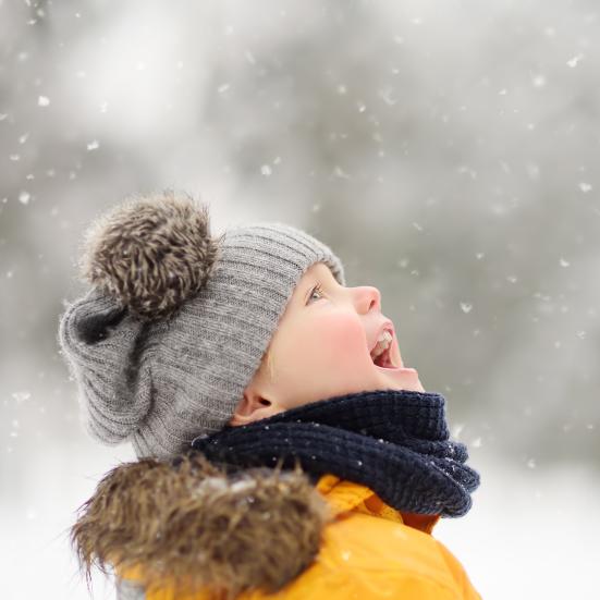 Glad dreng med hue står begejstret og ser mod himlen i snevejr.