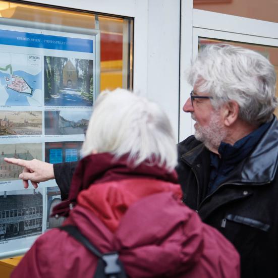 En frivillige peger på et plakat med gamle billeder og viser frem til en borger.