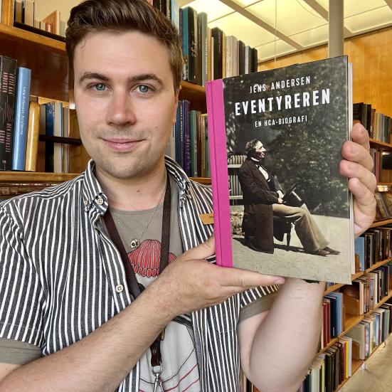 Bibliotekar Mathias Lyngs står og holder bogen "Eventyreren" på Nyborg Bibliotek.