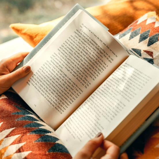 Billede til Read Hour. To hænder holder en opslået roman, der hvilker i skødet på læseren.