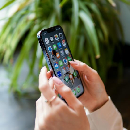 Hænder holder en smartphone, hvor man kan se alle de mange app-ikoner.