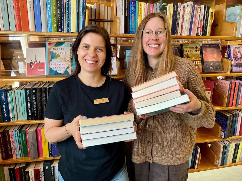 Bibliotekarer Marianne Wismar Mühring og Johanne Søndergaard Louv står med hver deres bogstak og smiler.