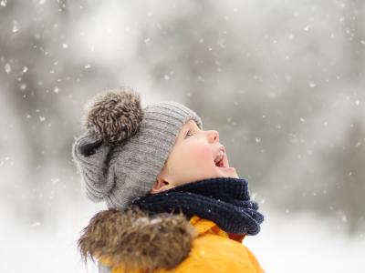 Glad dreng med hue står begejstret og ser mod himlen i snevejr.