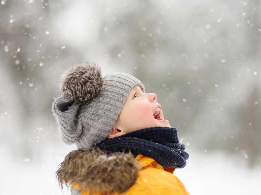 Glad dreng med hue står begejstret og ser mod himlen i snevejr.