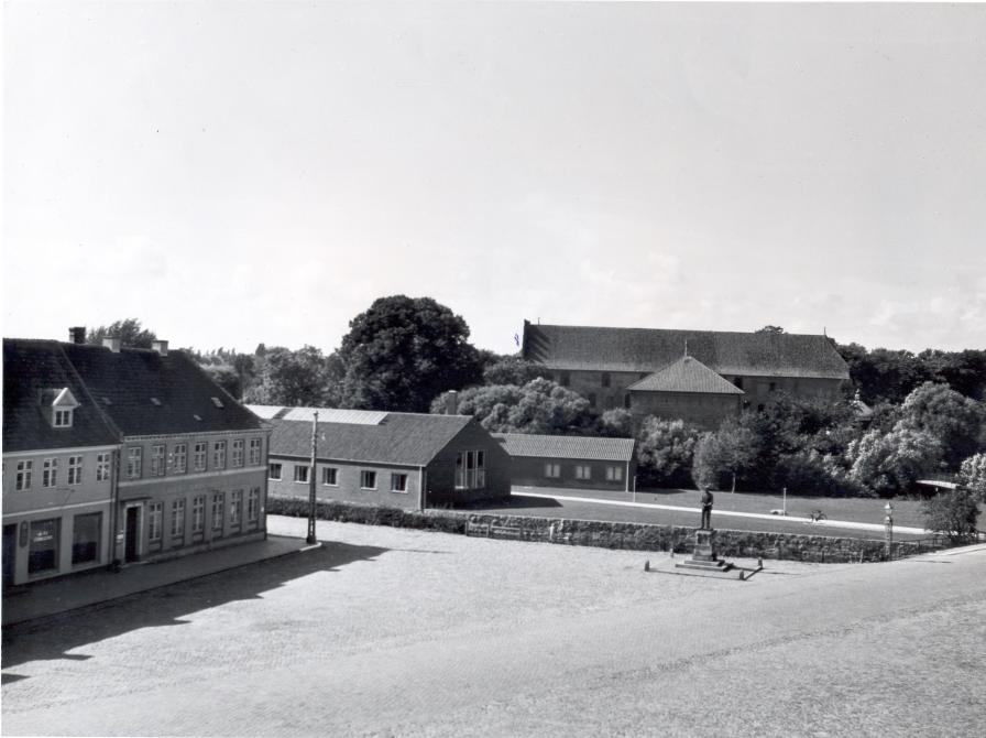 Nyborg Bibliotek set fra Rådhuset. Her ses det tydeligt, hvordan facaden på den store bygning flugter med bygninger på Torvet og den lille bygning ligger nærmest parallelt med den gamle vagttårn foran Nyborg Slot.