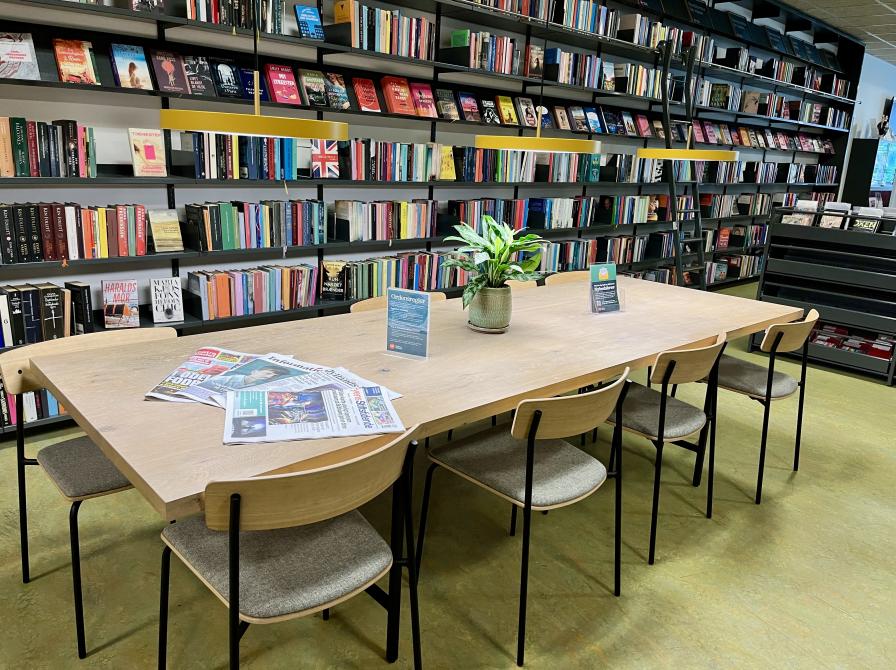 Et lyst bord med otte stole og en grøn plante i midten.  På Ørbæk Bibliotek er der plads til at du kan sidde og arbejde eller mødes med vennerne, strikkeklubben eller læseklubben m.m.