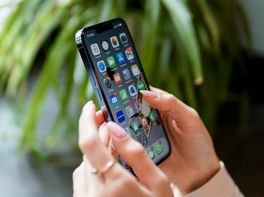 Hænder holder en smartphone, hvor man kan se alle de mange app-ikoner.